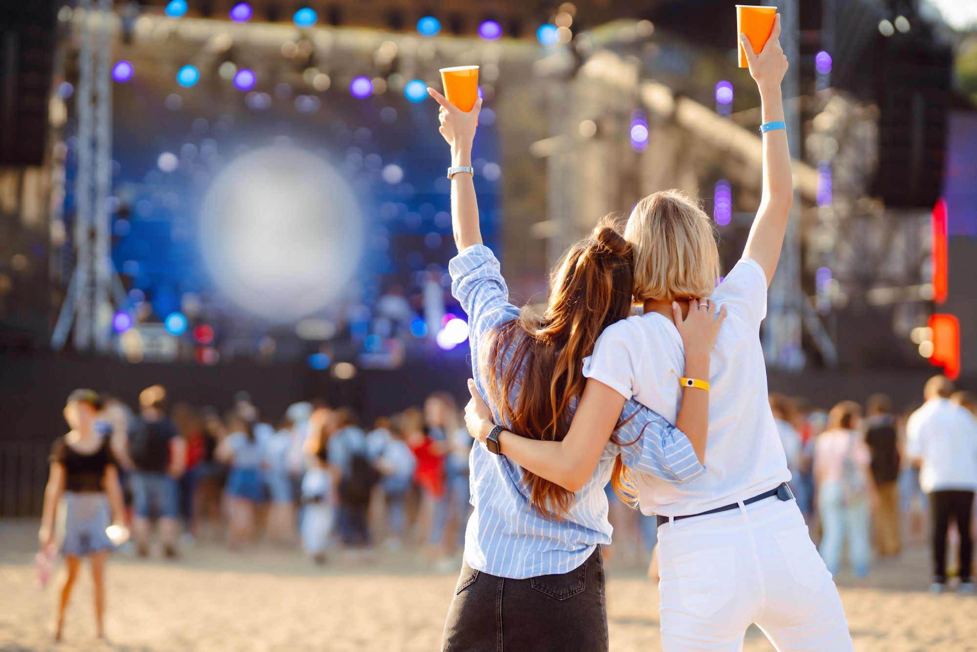 Festivalbezoekers met bekertjes en polsbandjes voor een podium